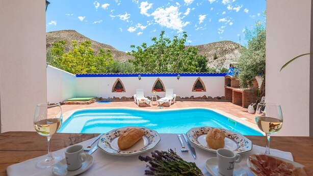 A poolside dining area with a view of a mountainous landscape, a table set with plates and glasses, and a chair.