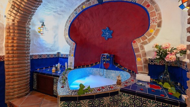 Un baño con una bañera de azulejos azules, una pared roja y un adorno con forma de corazón.