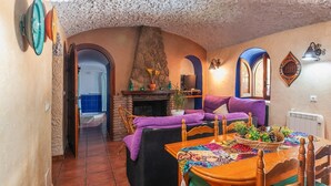 Ein gemütliches Wohnzimmer mit Kamin, einem Esstisch mit bunter Tischläufer und einer Couch mit violetten Kissen.