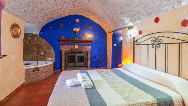 Ein Schlafzimmer mit Kamin aus Stein, einem Bett mit gestreifter Bettdecke und einer blauen Decke mit Sterndekorationen.