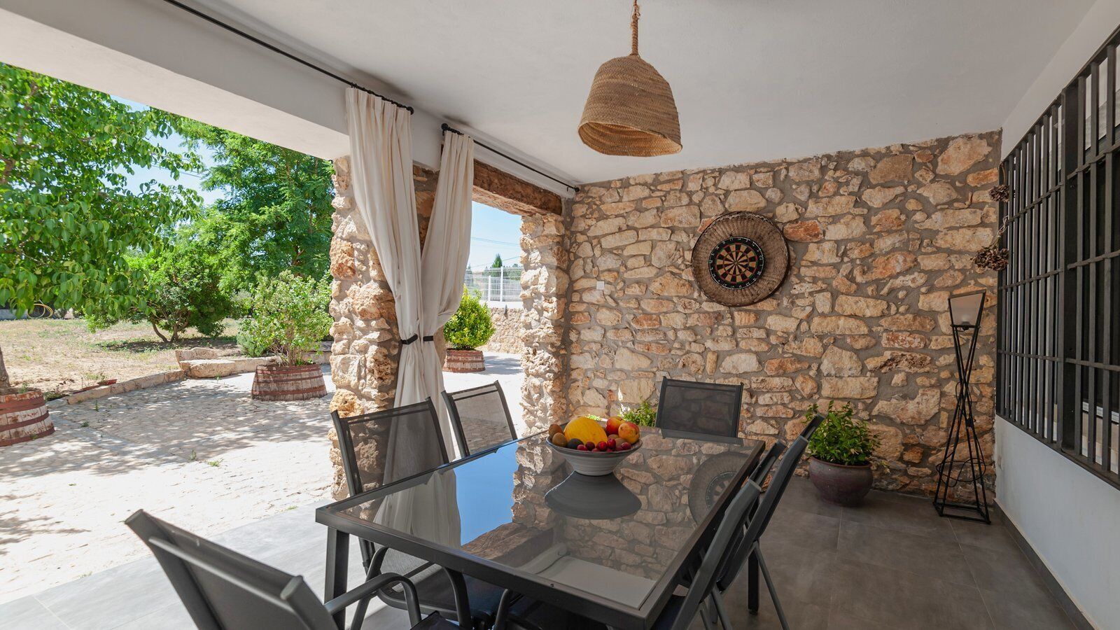 A patio with a stone wall, a table with chairs, a fruit bowl, and a hanging light fixture.
