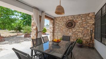 A patio with a stone wall, a table with chairs, a fruit bowl, and a hanging light fixture.