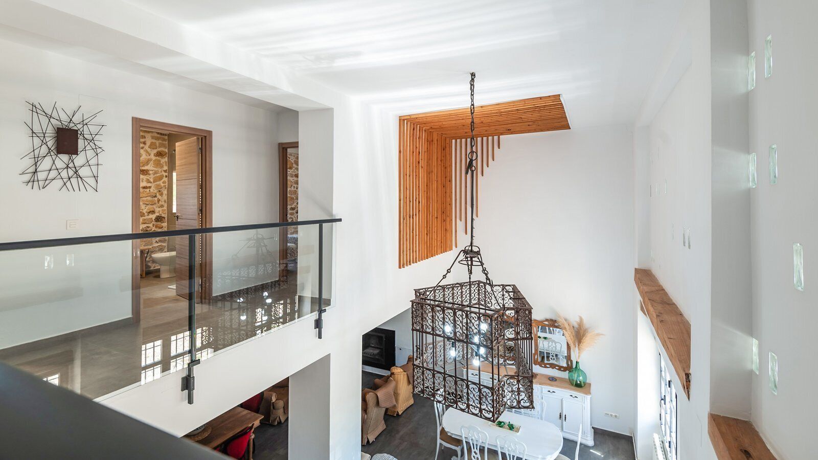 A modern interior with a glass balustrade, a hanging metal chandelier, and a stone wall.