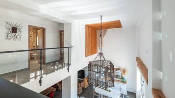 A modern interior with a glass balustrade, a hanging metal chandelier, and a stone wall.