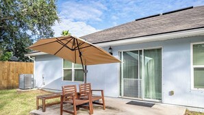 Une terrasse avec une table et des chaises en bois, un parasol, et une maison avec un toit et des fenêtres gris.