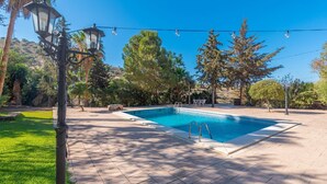 Ein rechteckiger Swimmingpool mit gefliestem Sonnendeck, umgeben von Bäumen und einer Laterne.