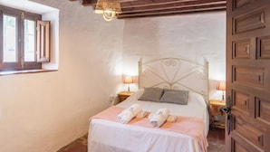 Ein Schlafzimmer mit einem Bett, zwei Nachttischen mit Lampen, einer Holztür und einem Fenster mit Vorhängen.