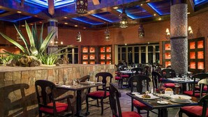 Een restaurantinterieur met bakstenen muren, stenen pilaren en rode bekleden stoelen. Tafels zijn gedekt met borden, glazen en bestek.