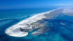 Een luchtbeeld van een kustgebied met een lang strand en helderblauw water.