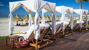 Een loungehoek aan het strand met houten ligbedden en rieten parasols.
