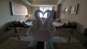 Een hotelkamer met een handdoekarrangement in de vorm van een hart, een sofa, een bed en een groot raam.