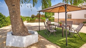 Eine Terrasse im Freien mit Tisch und Stühlen, einem Baum und einer Pergola, die Schatten spendet.