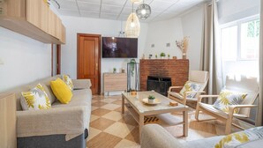 Ein Wohnzimmer mit einer Couch, Sesseln, einem Couchtisch, einem Kamin und einem an der Wand befestigten Fernseher.