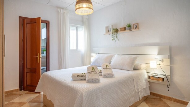 Ein Hotelzimmer mit Bett, Nachttisch, Lampe und einem Fenster mit Vorhängen.