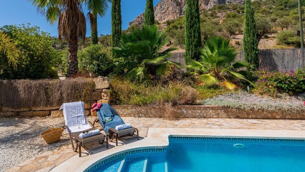 Un espace aménagé au bord de la piscine, avec des chaises longues et un mur en pierre.