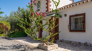 Un bâtiment doté d’une cour pavée de pierres, d’un pot de fleurs orné de fleurs roses et d’une fenêtre protégée par une grille en métal.