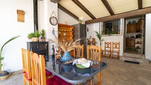 Uma sala de jantar com mesa de vidro, cadeiras de madeira, um vaso azul e uma cesta de pão.