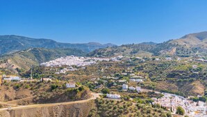 Un pueblo costero con edificios blancos, una carretera sinuosa y colinas al fondo.