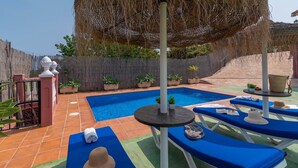 A swimming pool with blue lounge chairs and a table, surrounded by potted plants and a wooden fence. - Villa Mariposas Torrox by Ruralidays (Málaga)