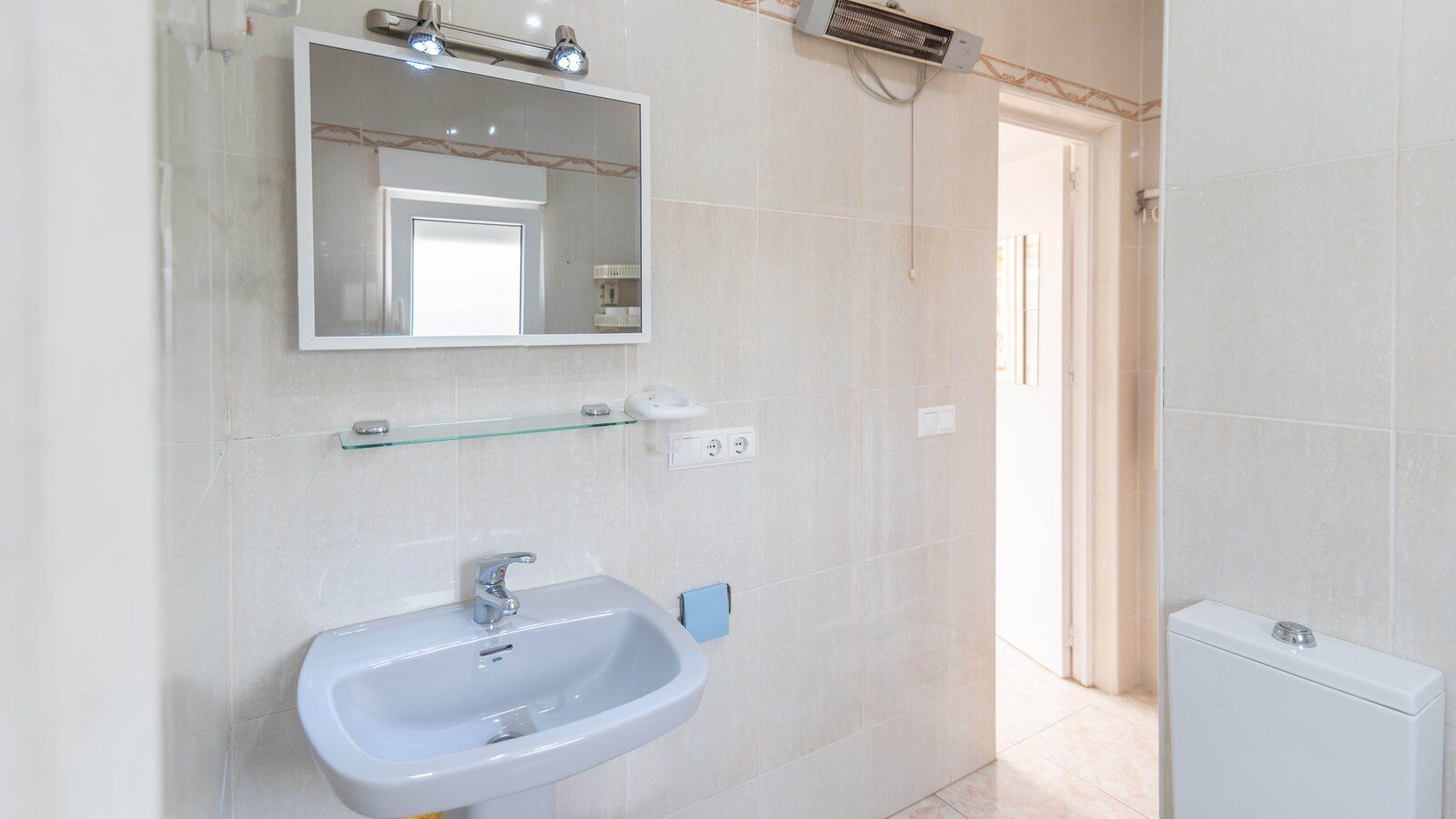 A bathroom with a white sink, mirror, and a small glass shelf.