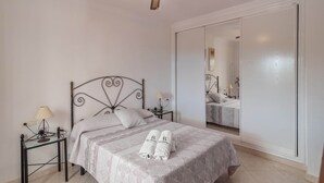 A neatly made bed with a patterned bedspread and two towels, a bedside table with a lamp, and a large mirror on the wall. - Villa Mariposas Torrox by Ruralidays (Málaga)