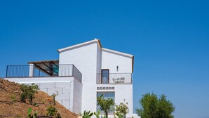 Ein modernes, zweistöckiges Gebäude mit weißer Fassade, einem Balkon im oberen Geschoss und einer Treppe, die zu diesem führt.