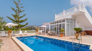 Zona de piscina amb vista clara al mar, edifici blanc amb grans finestres i mobiliari d'exterior.