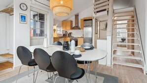 Una cocina moderna con una isla central, una zona de comedor con cuatro sillas y un dormitorio entrepiso con escalera de madera.
