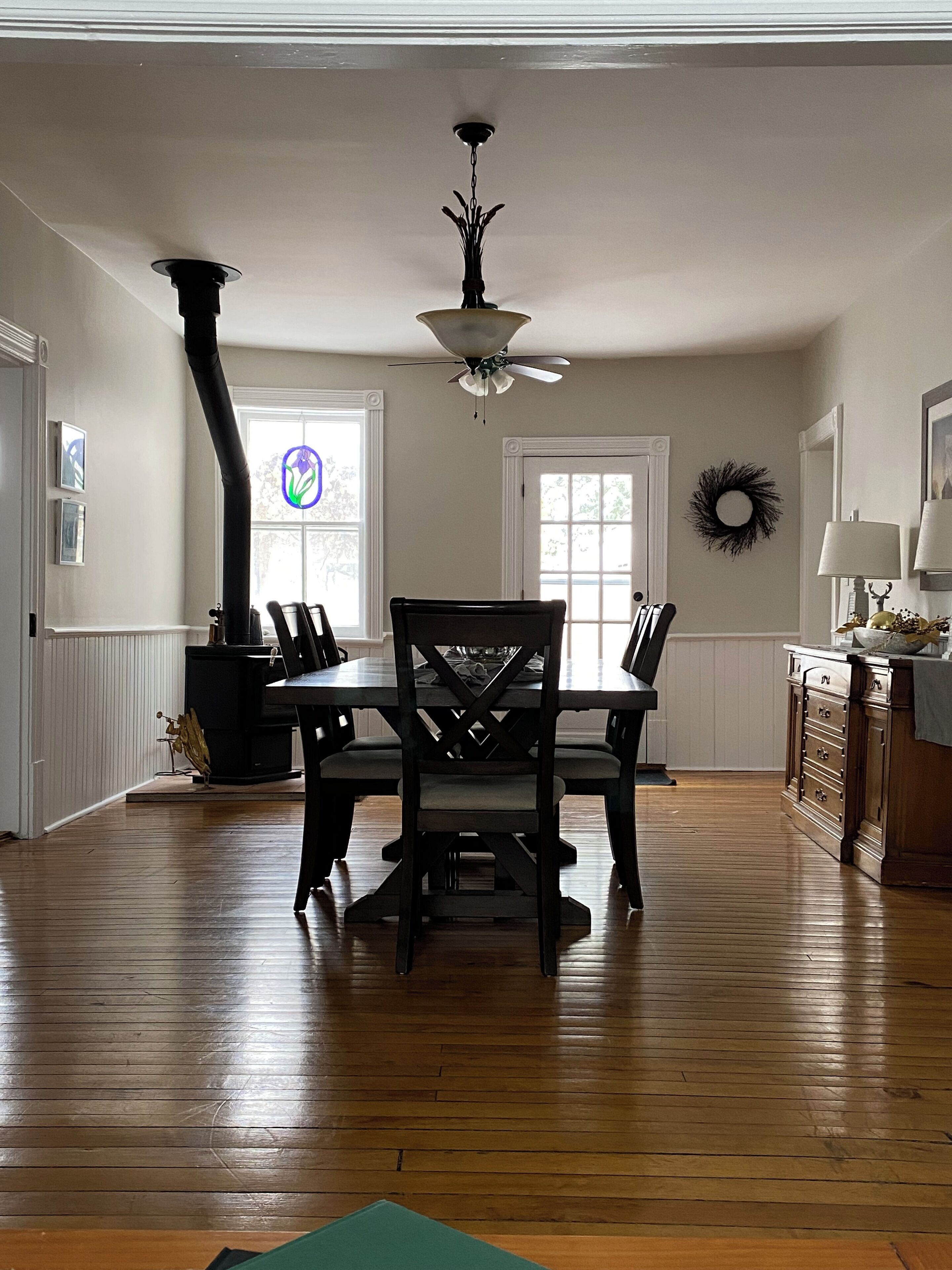 A dining area with a wooden table and chairs, a ceiling fan, and a window with a stained glass design.