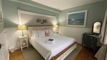 A neatly arranged bedroom with a large bed, two bedside tables, a dresser, and a painting on the wall.