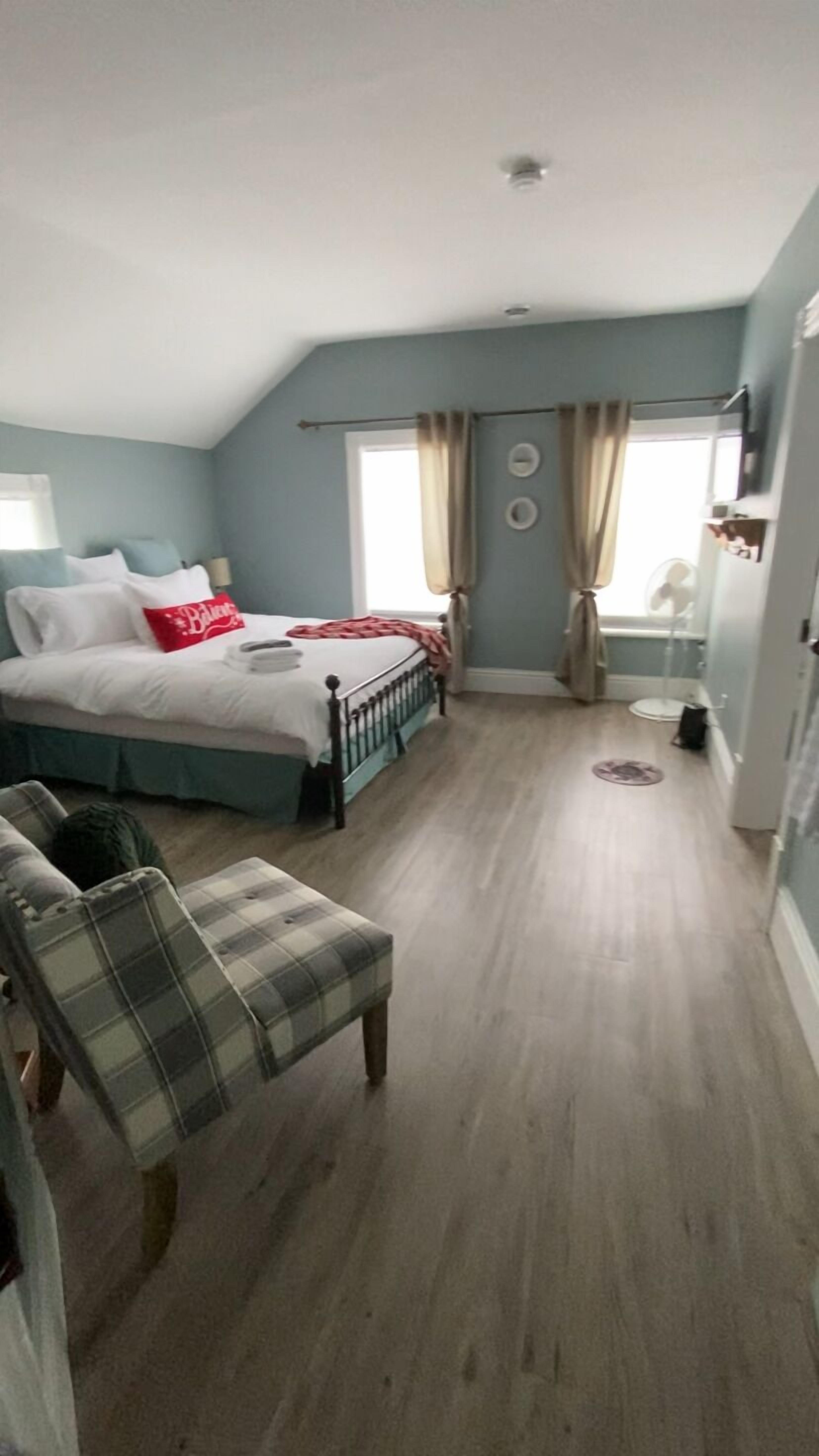 Un dormitorio con una cama, una silla, un ventanal y una puerta.