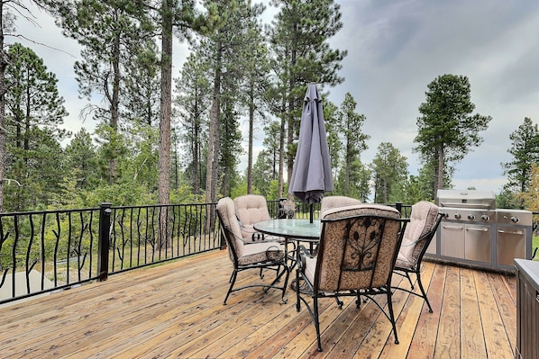 A wooden deck with a round table and chairs, surrounded by a black metal railing.