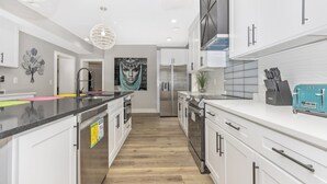 Une cuisine moderne avec des meubles blancs, un plan de travail noir et un réfrigérateur en acier inoxydable.