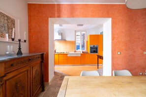 A modern kitchen with orange cabinets, a wooden dining table, and a white chair. - Boutique Apartment Near Spanish Steps (Roma)