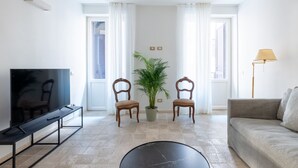 A living room with a flat-screen TV, two wooden chairs, a potted plant, a sofa, and a lamp. - Boutique Apartment Near Spanish Steps (Roma)