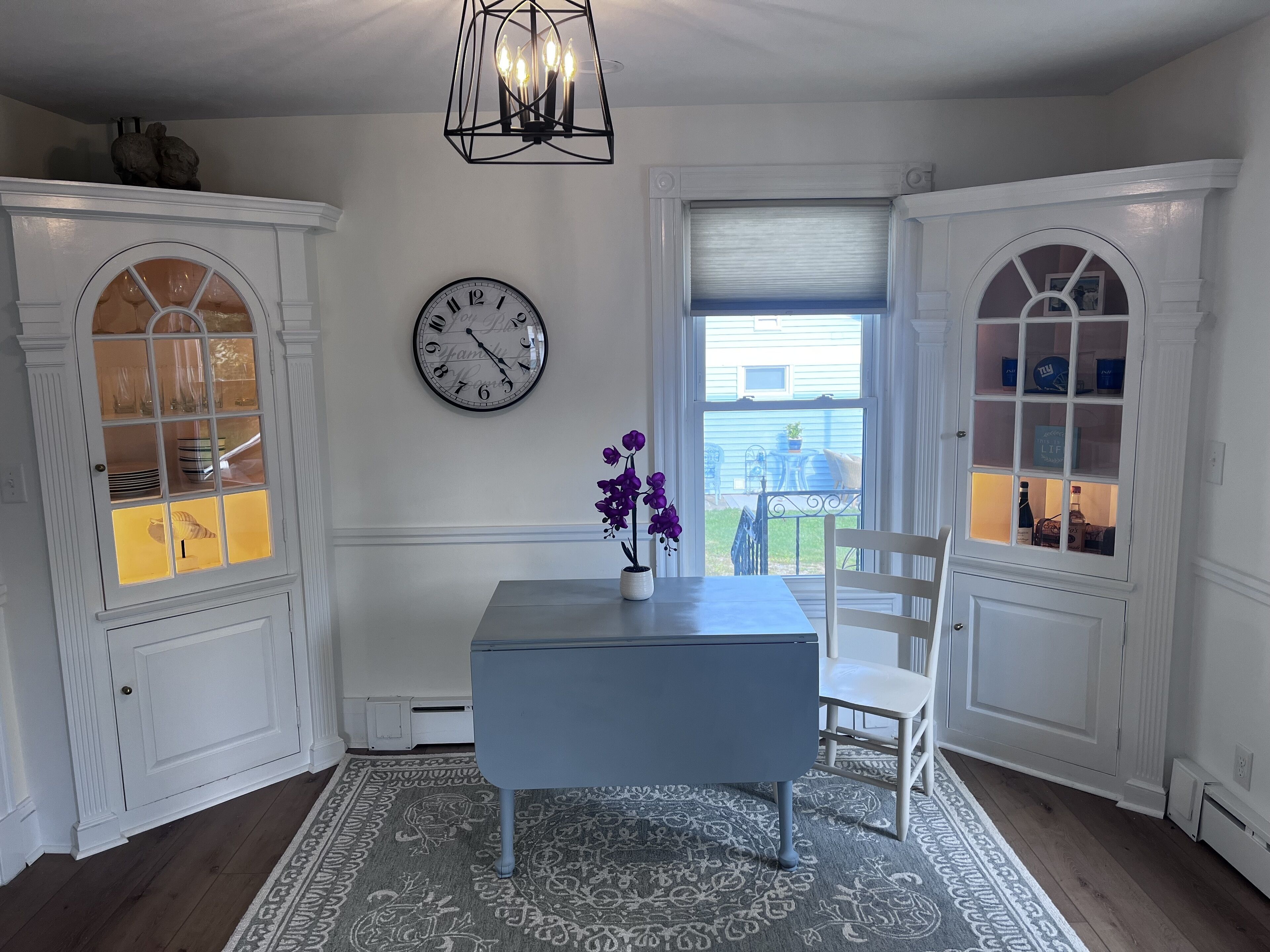 Un comedor con una mesa, sillas, un reloj y una ventana con vistas.