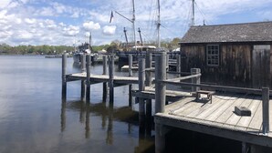 Un muelle de madera con un pequeño edificio, barcos y agua tranquila.