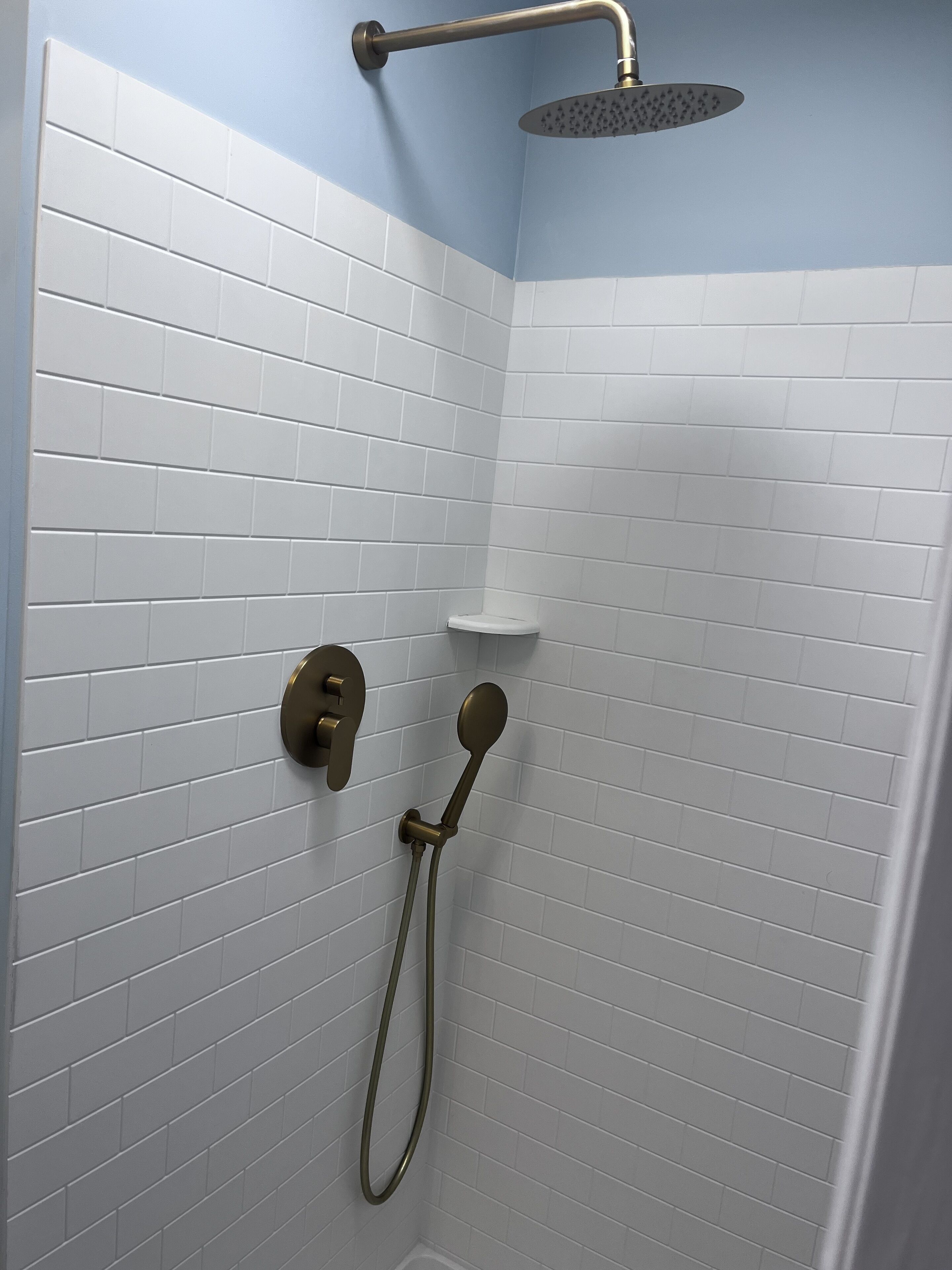 A shower area with white tiled walls and a showerhead.