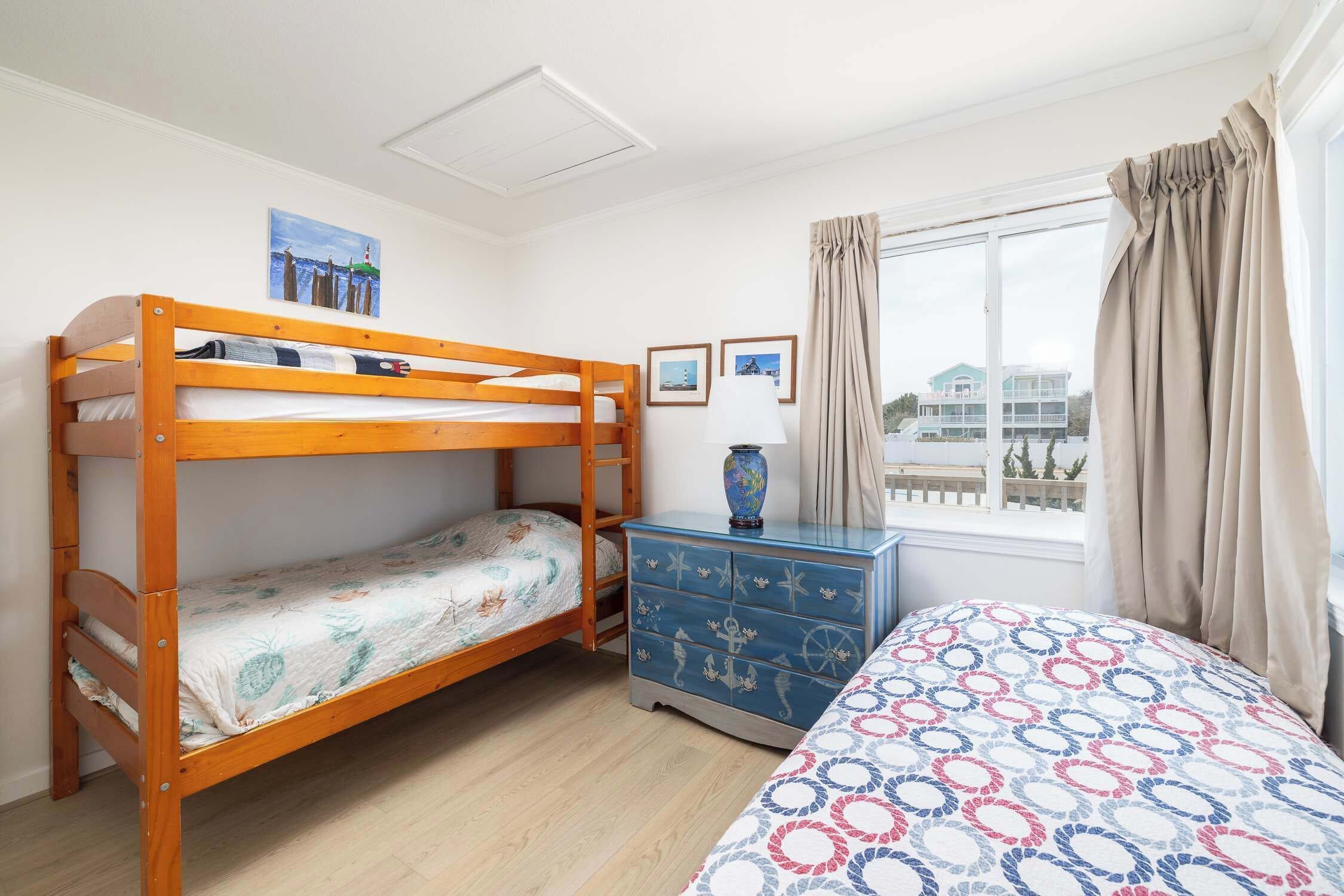 A room with a bunk bed, a dresser, and a window with curtains.