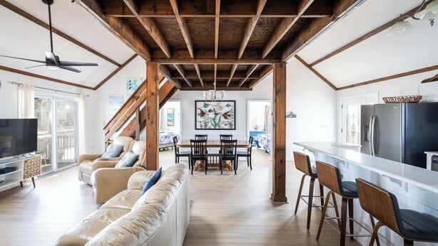 A spacious living area with a wooden ceiling, a sofa, a TV, and a dining area with chairs and a table. - New 2026 Renovations Retreat Just Steps to Beach! (Kitty Hawk)