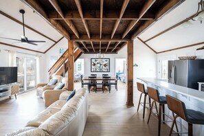Amplia sala de estar con techo de madera, un sofá, un televisor y un comedor con sillas y una mesa.