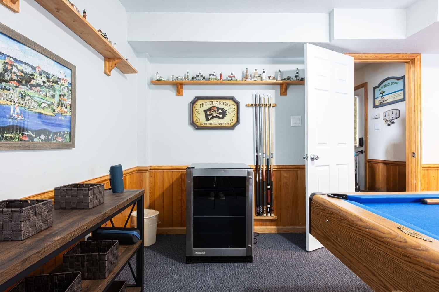 A pool room with a pool table, a refrigerator, and a wall-mounted shelf with miniature lighthouses.