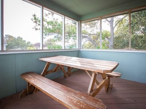 Una mesa de picnic de madera con bancos en un espacio exterior cubierto con ventanas amplias.