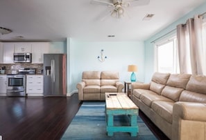 Ein modernes Wohnzimmer mit einem beigen Sofa, einem Holztisch und einer Küche im Hintergrund.