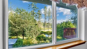 Ikkunasta avautuu näkymä puilla ympäröityyn lammikkoon ja sen vieressä olevalle puukannelle.