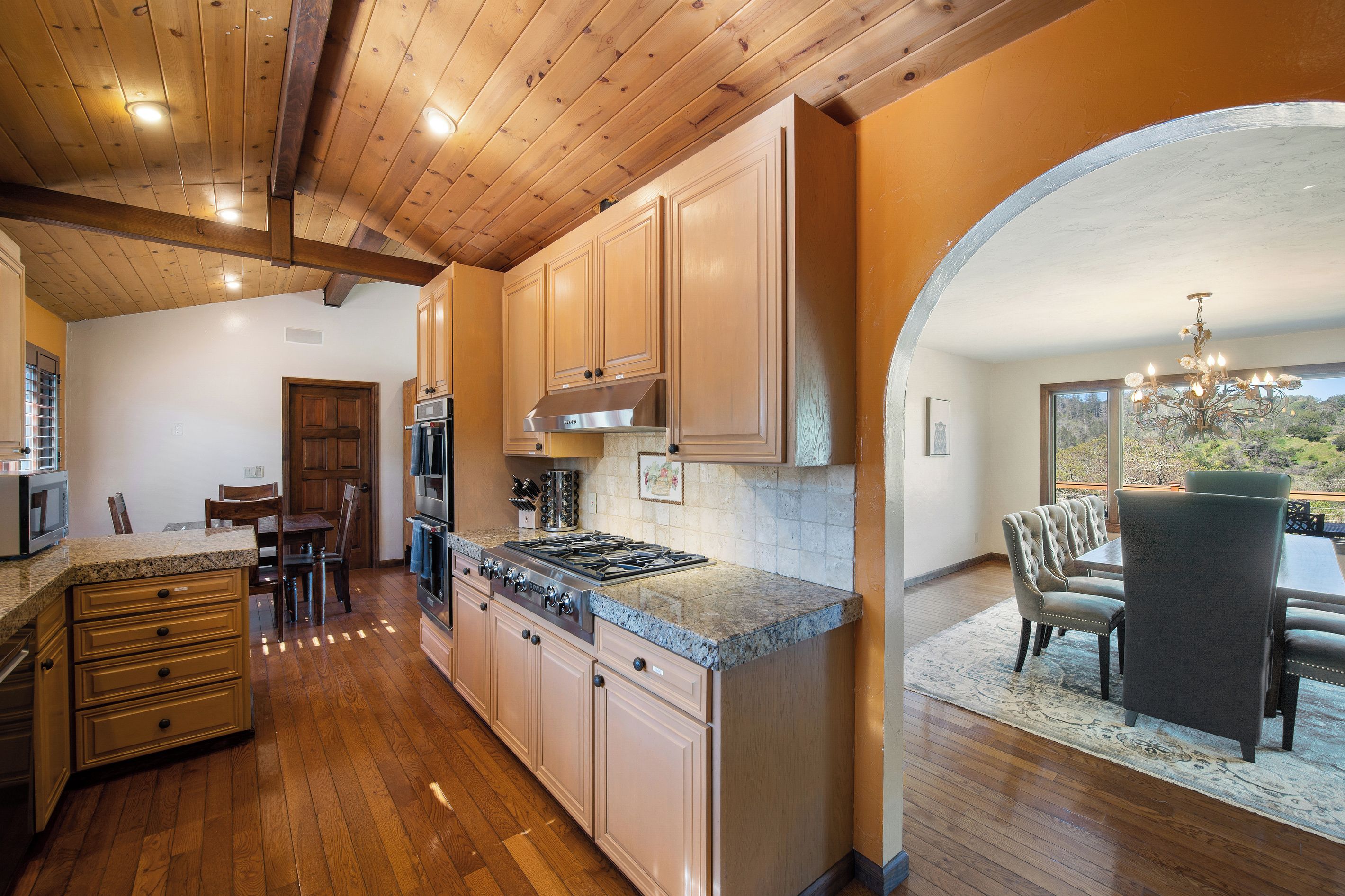 A kitchen with wooden cabinets, a stove, and a dining area with a table and chairs.