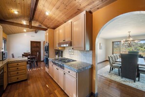 A kitchen with wooden cabinets, a stove, and a dining area with a table and chairs. - Farpoint: Heated Infinity Pool, Mountain Views (Santa Rosa)