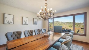 Un coin repas avec une table en bois et six chaises, un lustre et des tableaux représentant des animaux accrochés au mur.