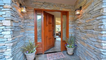 A stone-walled entrance with a wooden door, potted plants, and a welcome mat.