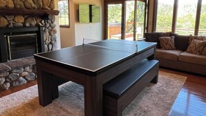 Une table de billard dans une pièce dotée d’une cheminée en pierre, d’un canapé et de grandes fenêtres.